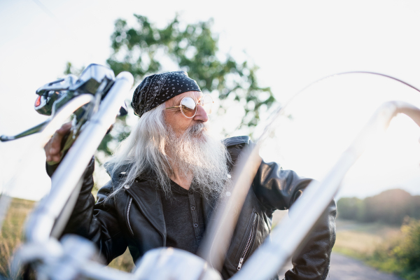 A senior man traveller with motorbike and sunglasses in countryside.