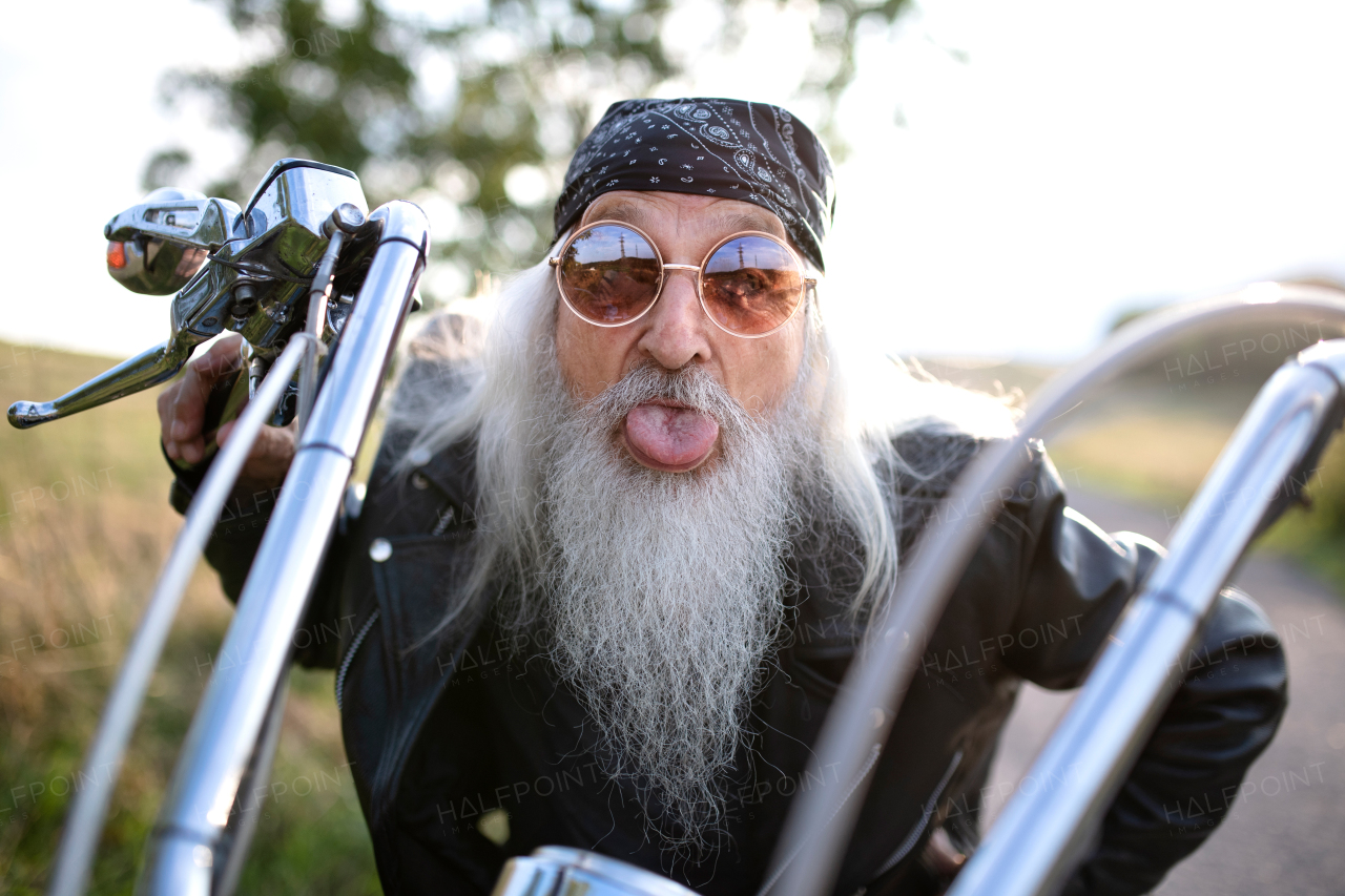 Senior man traveller with motorbike and sunglasses in countryside, having fun.