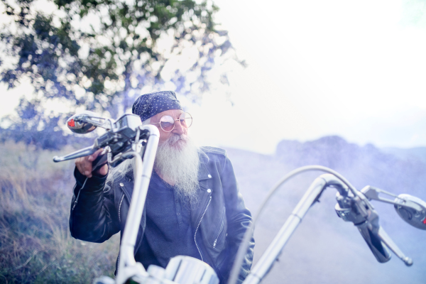 A senior man traveller with motorbike and sunglasses in countryside.