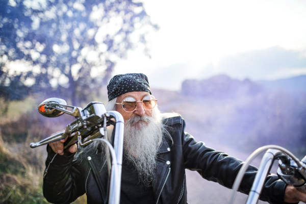 A senior man traveller with motorbike and sunglasses in countryside.