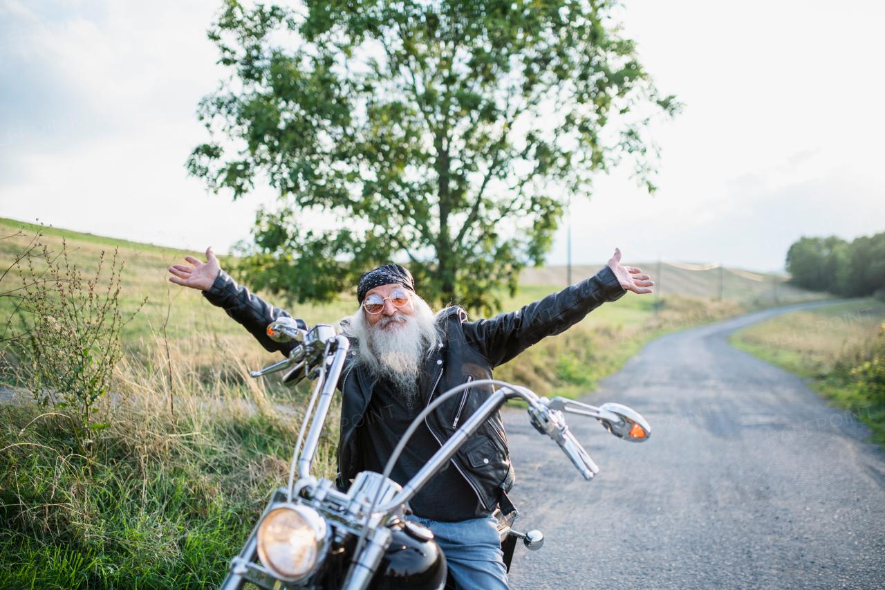 A senior man traveller with motorbike and sunglasses in countryside, stretching arms.