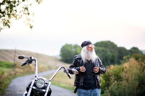 A senior man traveller with motorbike and sunglasses in countryside.