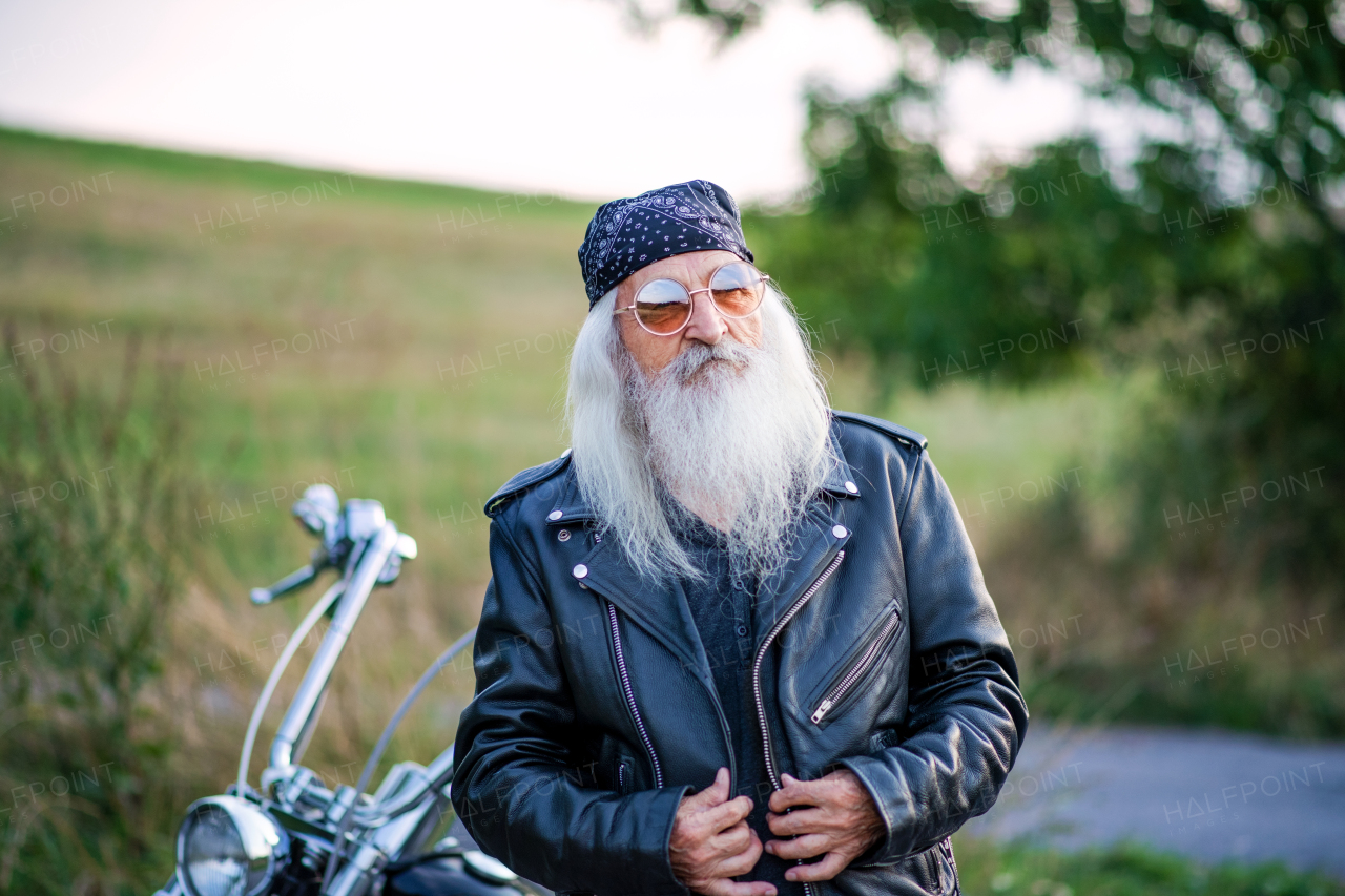 A senior man traveller with motorbike and sunglasses in countryside.