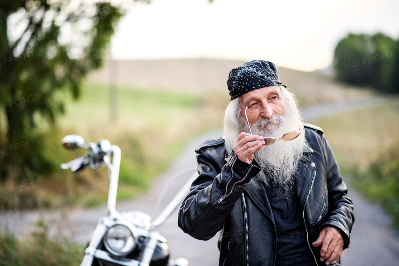 A senior man traveller with motorbike and sunglasses in countryside.