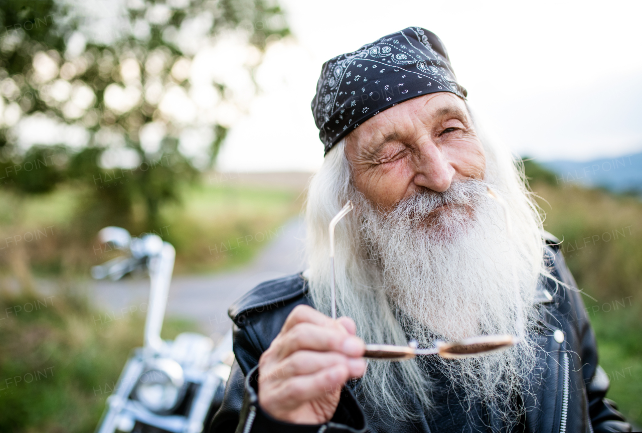 Senior man traveller with motorbike and sunglasses in countryside, winking.