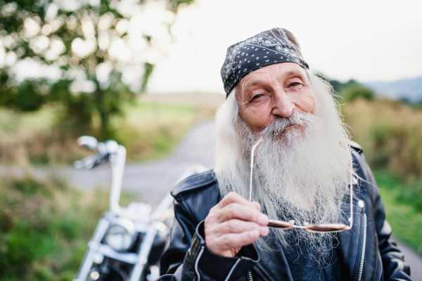 A senior man traveller with motorbike and sunglasses in countryside.