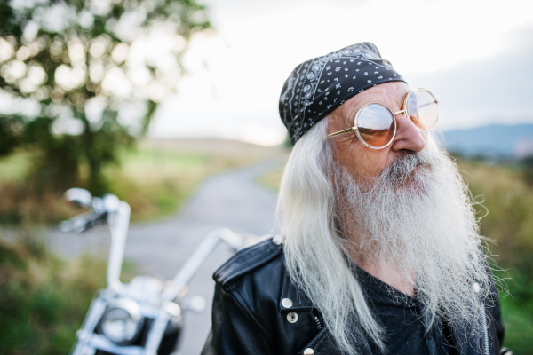 A senior man traveller with motorbike and sunglasses in countryside.