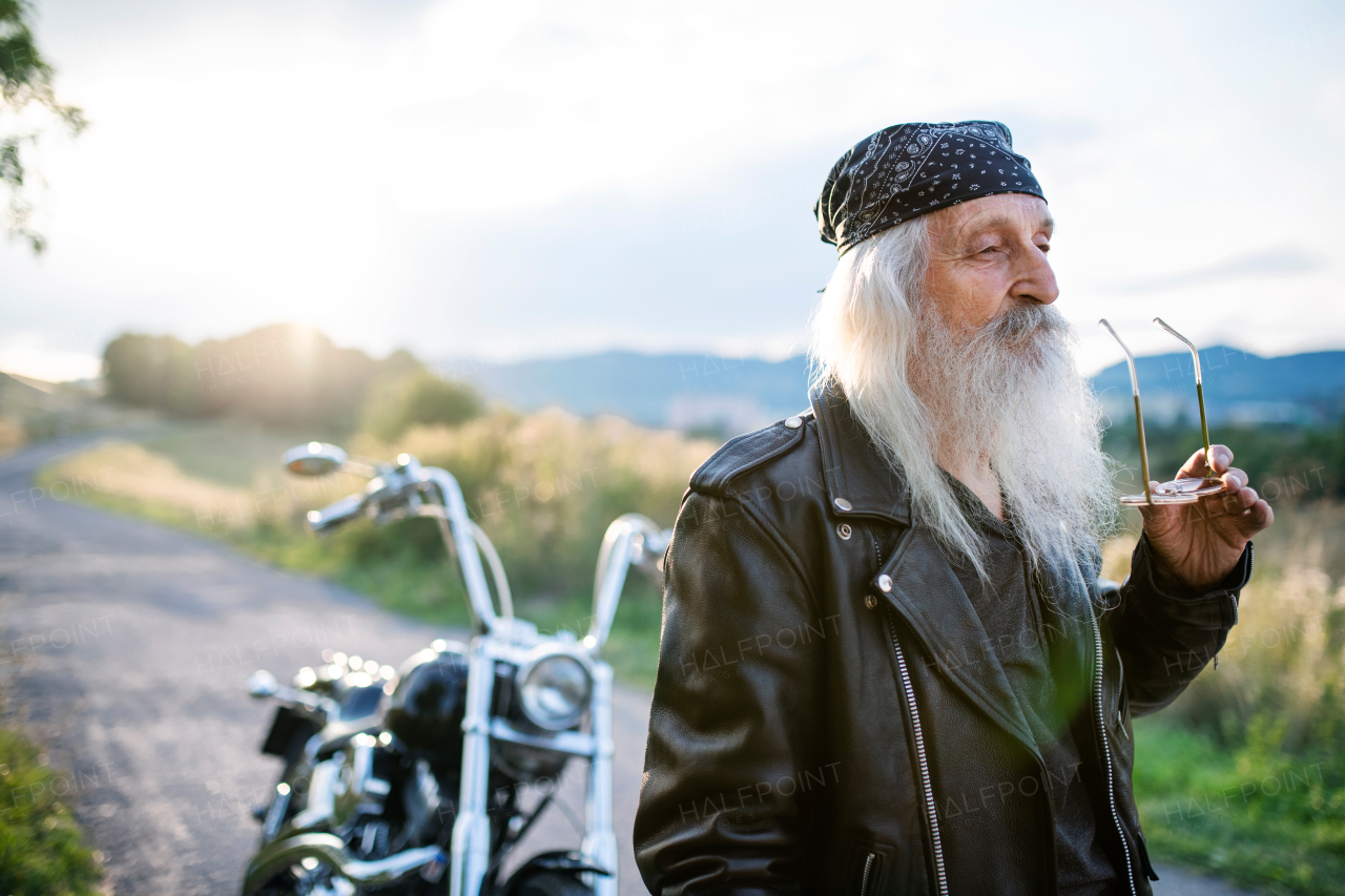 A senior man traveller with motorbike and sunglasses in countryside.