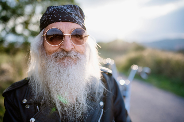 A senior man traveller with motorbike and sunglasses in countryside.