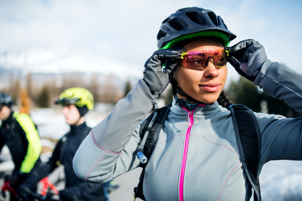 Group of mountain bikers standing on road outdoors in winter, putting on sunglasses.