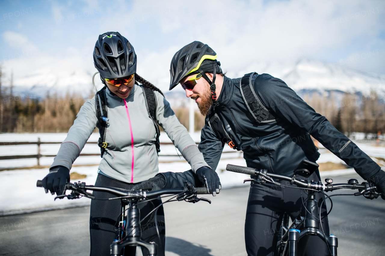 Two mountain bikers riding on road outdoors in winter, talking.