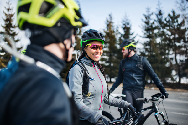 A group of young mountain bikers standing on road outdoors in winter, talking.