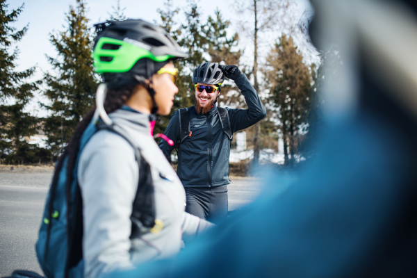 A group of young mountain bikers standing on road outdoors in winter, talking.