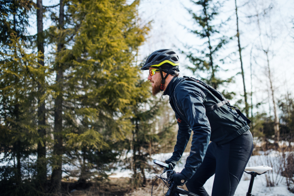 A side view of mountain biker riding in snow outdoors in winter nature.