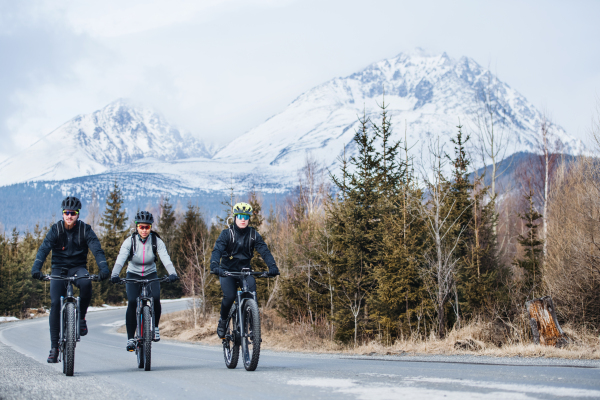 A group of young mountain bikers riding on road outdoors in winter.