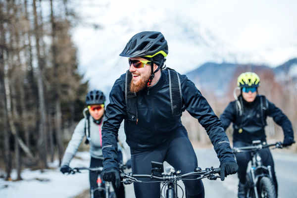 A front view of group of young mountain bikers riding on road outdoors in winter.