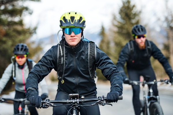 A group of young mountain bikers riding on road outdoors in winter.