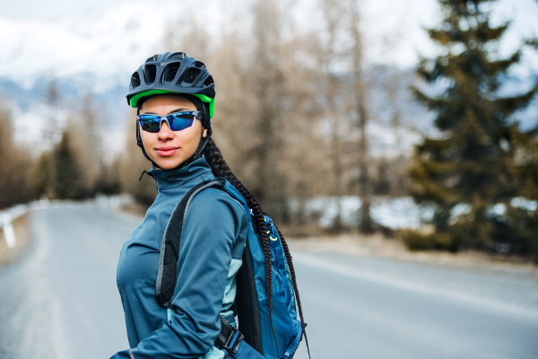 A happy female mountain biker standing on road outdoors in winter nature.