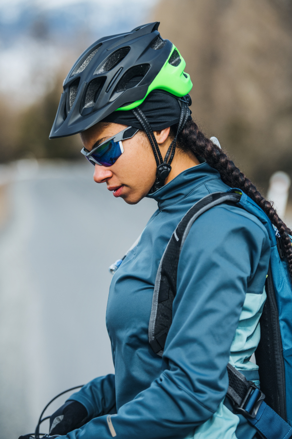 A side view of female mountain biker standing on road outdoors in winter nature.