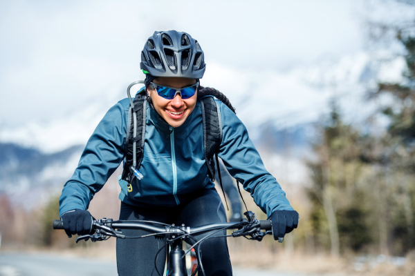 Front view of cheerful female mountain biker riding in snow outdoors in winter nature.