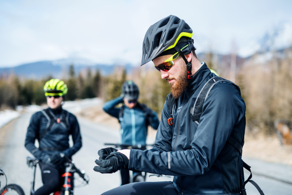 A group of young mountain bikers standing on road outdoors in winter.