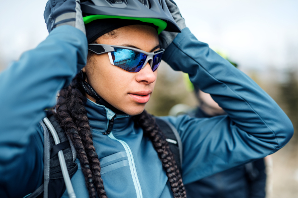 Female mountain biker standing on road outdoors in winter, putting on sunglasses.