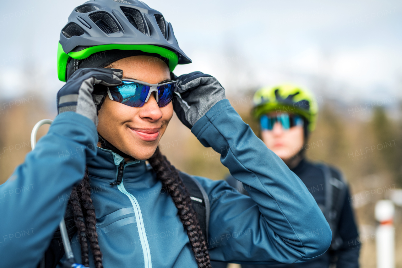 Two mountain bikers standing on road outdoors in winter, putting on sunglasses.