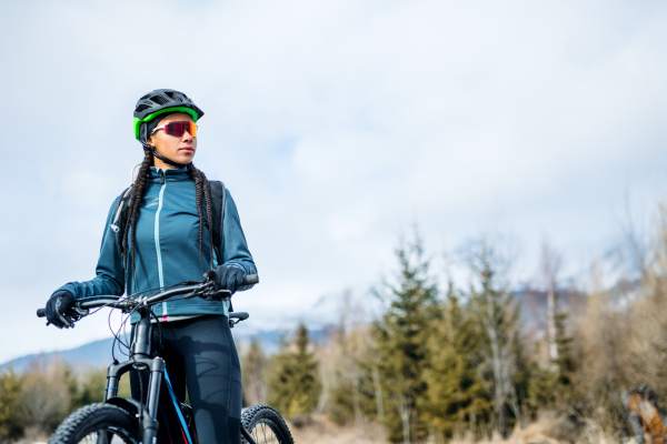 A happy female mountain biker standing outdoors in winter nature. Copy space.