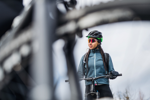 Female mountain biker with sunglasses standing on road outdoors in winter.