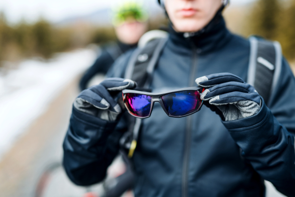 A midsection of mountain biker standing outdoors in winter, putting on sunglasses.