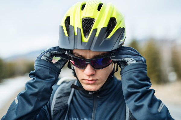 A close-up of mountain biker with sunglasses standing outdoors in winter.