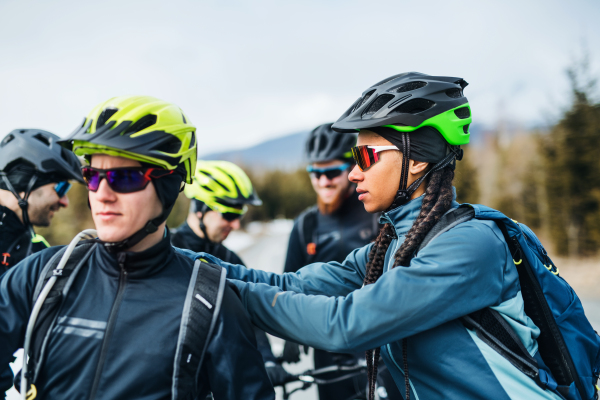 A group of young mountain bikers standing on road outdoors in winter, talking.