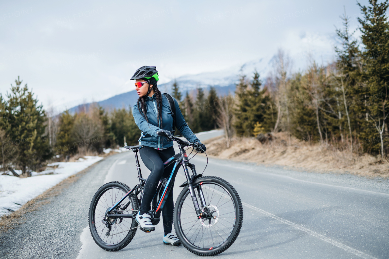 A female mountain biker standing on road outdoors in winter nature. Copy space.