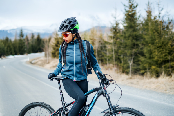 A female mountain biker standing on road outdoors in winter nature. Copy space.