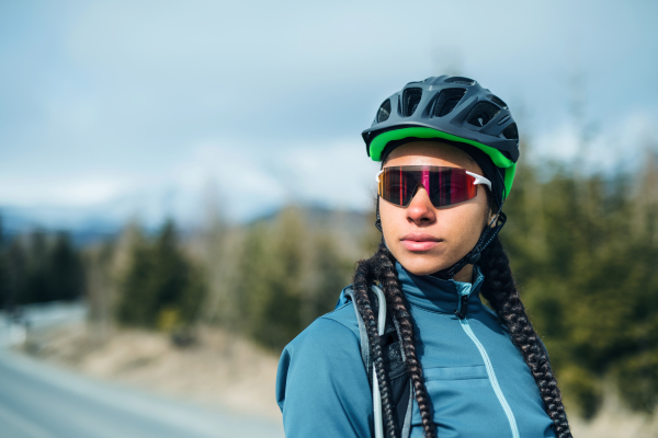 A happy female mountain biker standing on road outdoors in winter nature.