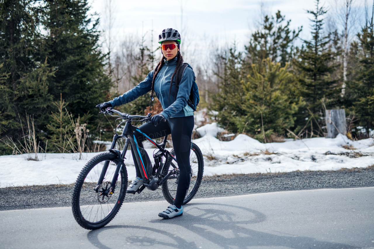 A female mountain biker standing on road outdoors in winter nature. Copy space.