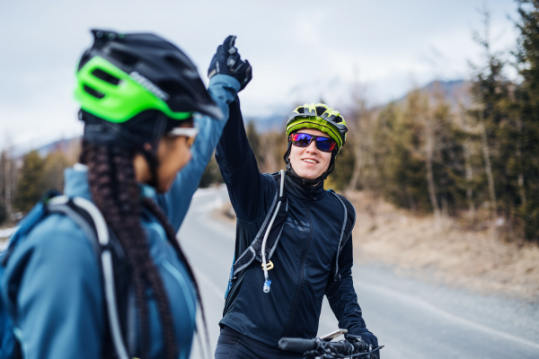 Two mountain bikers standing on road outdoors in winter, giving high five when resting.