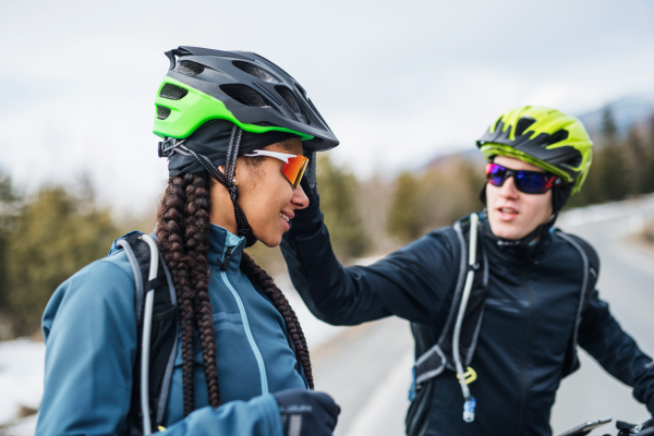 Two mountain bikers riding on road outdoors in winter, talking.