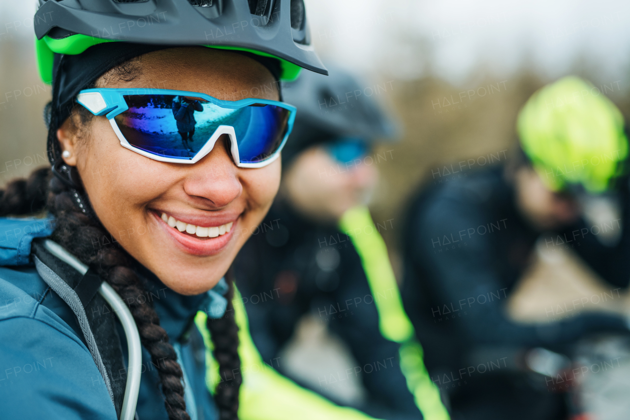 Female mountain biker with sunglasses and friends standing on road outdoors in winter.