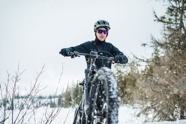 A front view of mountain biker riding in snow outdoors in winter nature.