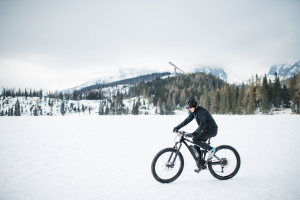 A side view of mountain biker riding in snow outdoors in winter nature.