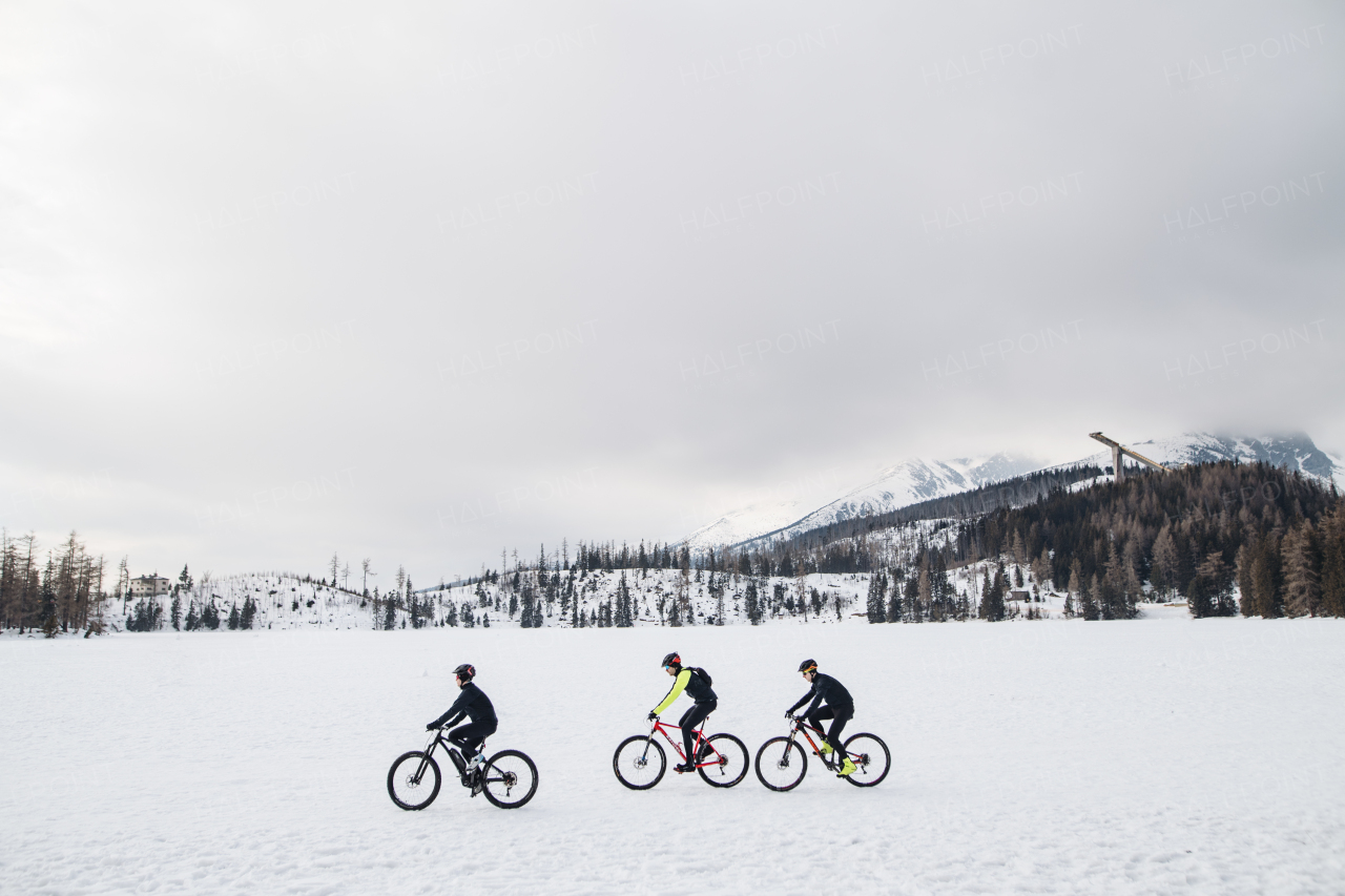 A side view of group of mountain bikers riding outdoors in winter.