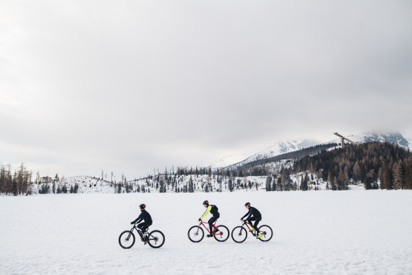 A side view of group of mountain bikers riding outdoors in winter.