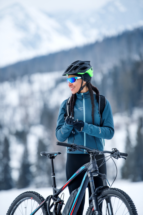 A happy female mountain biker standing outdoors in winter nature.