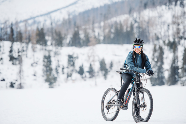 Female mountain biker with bicycle standing outdoors in winter nature. Copy space.