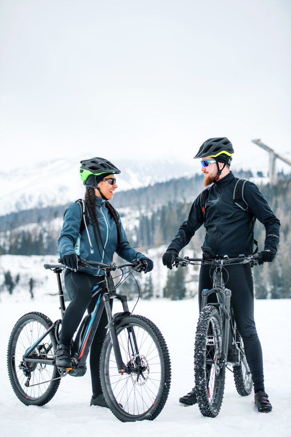 Two mountain bikers with bicycles resting outdoors in winter, talking.