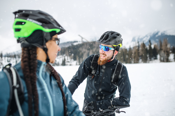 Two mountain bikers with bicycles on road outdoors in winter, talking when resting.