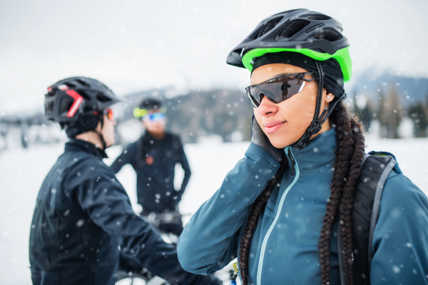 Female mountain biker with sunglasses and friends standing outdoors in winter.