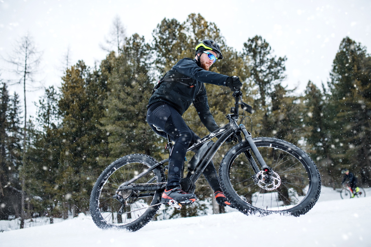 A side view of mountain biker riding in snow outdoors in winter nature.