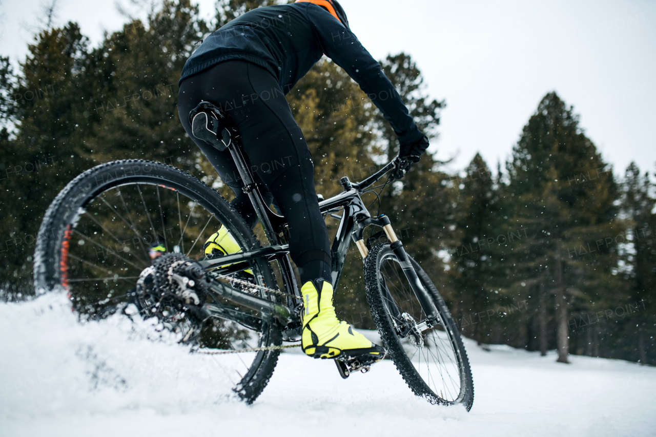 A midsection of mountain biker riding in snow outdoors in winter.